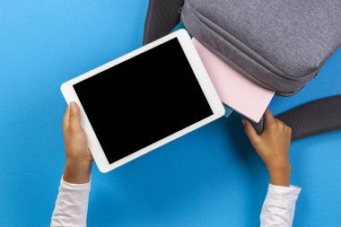 Çocuk elleri açık mavi arka plan üzerinde gri sırt çantasıtablet bilgisayar alarak