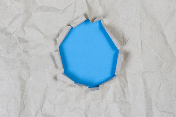 Hole in old crumpled paper with light blue background inside