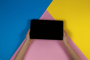 Tablet bilgisayarda mavi pembe ve sarı arka plan ile çocuk el