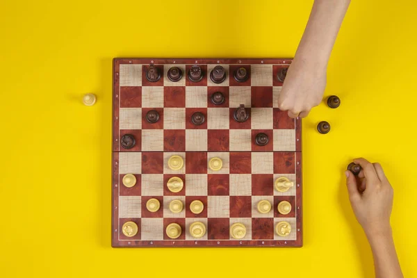 Kids hands over a chessboard playing chess game on yellow background, top view — Stock Photo, Image