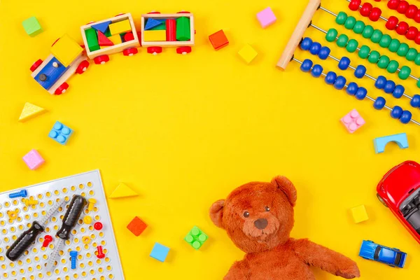 Giocattoli per bambini sfondo. Orsacchiotto, treno in legno, blocchi colorati, kit attrezzi giocattolo, auto, abaco su sfondo giallo — Foto Stock