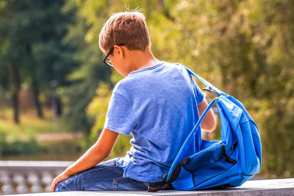 Niño cansado con mochila sentado al aire libre después de la escuela — Foto de Stock