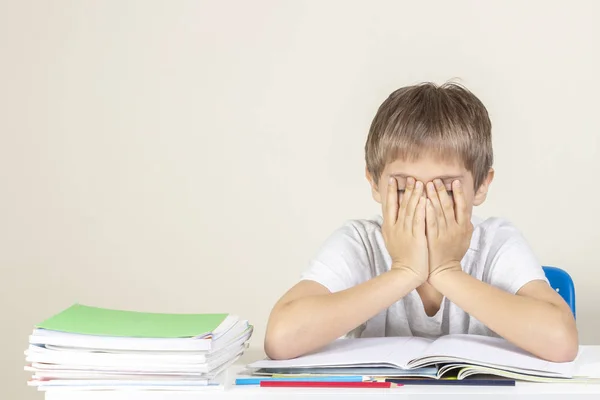 Szomorú fáradt ideges iskolás, amely szembe a kezével ült az asztal közelében a halom iskolai könyvek és notebookok — Stock Fotó