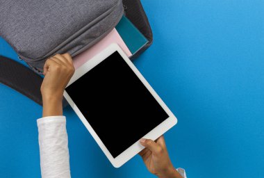 Çocuk elleri açık mavi arka plan üzerinde gri sırt çantasıtablet bilgisayar alarak