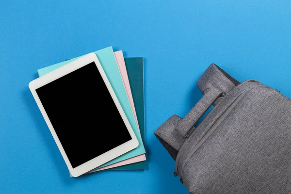 E-öğrenme kavramı - renkli kitap ve dizüstü bilgisayar yığını ve mavi arka plan sırt çantası üstüne boş tablet bilgisayar