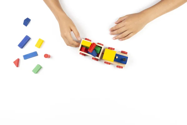 Kid hands playing with toy train and colorful wooden cube blocks on white table background. Top view — Stock Photo, Image