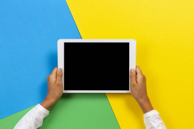 Sarı, mavi ve yeşil arka planda tablet bilgisayar ile Çocuk eller
