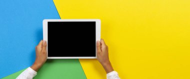 Sarı, mavi ve yeşil arka planda tablet bilgisayar ile Çocuk eller