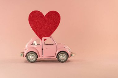 Vilnius, Litvanya - 09 Eylül 2019: Pastel pembe arka plan üzerinde kırmızı kalpli küçük retro oyuncak model araba. Aşk, dostluk, sevgililer günü, teslimat, bağış kavramı