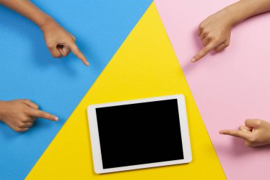Mavi, pembe ve sarı arka plandaki boş tablet bilgisayara parmak la işaret eden çocuklar