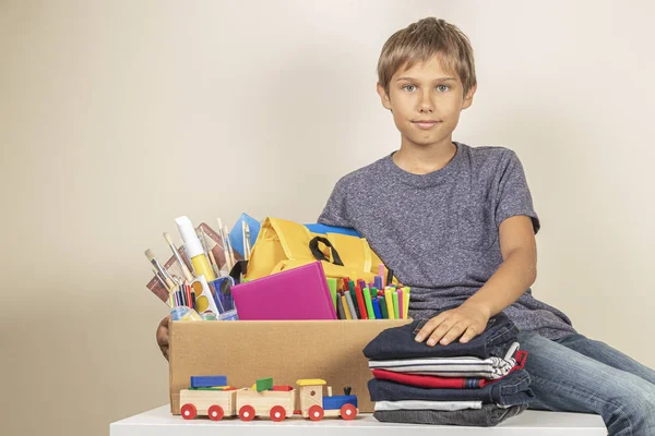 Concepto de donación. Niño sosteniendo donar caja con libros, lápices y útiles escolares —  Fotos de Stock