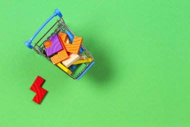 Mini alışveriş arabası yeşil arka planda renkli oyuncak yapboz tuğlalarıyla dolu.