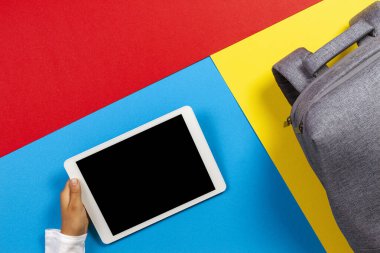 Renkli arka planda tablet bilgisayar ve gri sırt çantası ile çocuk ellerine üst görünüm