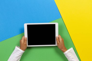Sarı, mavi ve yeşil arka planda tablet bilgisayar ile Çocuk eller