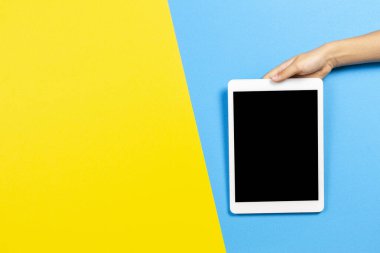 Sarı ve açık mavi zemin üzerinde tablet bilgisayarı olan çocuk eli