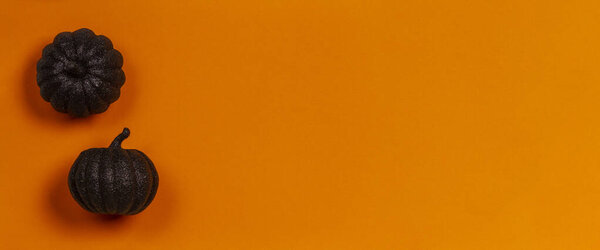 Minimal Halloween background. Decorative black shiny pumpkins on orange background. Top view