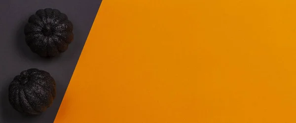 Fondo mínimo de Halloween. Calabazas decorativas negras brillantes sobre fondo naranja y negro. Vista superior — Foto de Stock