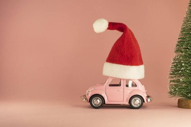 Kırmızı Noel Baba şapkası ve pastel pembe arka planda küçük Xmas ağacı olan pembe retro model bir araba. Vilnius, Litvanya, Eylül 09, 2019