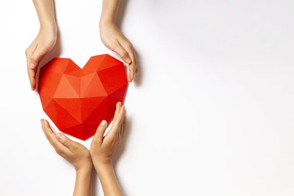 Two persons hands with red polygonal paper heart shape over white background