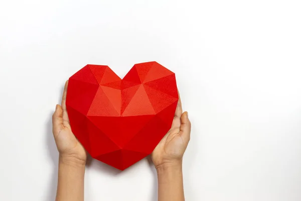 Hands holding red polygonal paper heart shape over white background — Stock Photo, Image