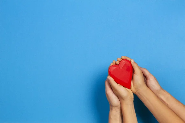 Adulto e criança mãos segurando coração vermelho sobre fundo azul. Amor, saúde, família, seguro, conceito de doação — Fotografia de Stock