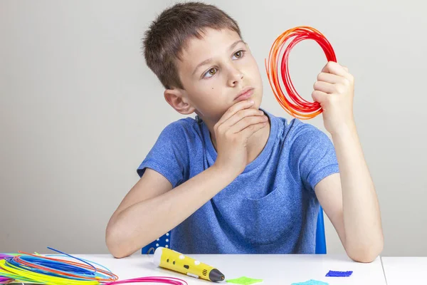 Kid segurando caneta 3d e filamentos coloridos para caneta 3 d e pensando o que criar — Fotografia de Stock