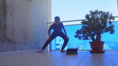 Tablet bilgisayarlı genç çocuk balkonda spor egzersizleri yapıyor. Spor, sağlıklı yaşam tarzı, evde boş vakit geçirme.