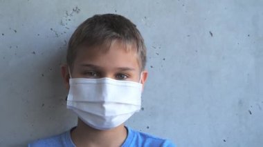 Çocuk tıbbi koruyucu maskesini çıkarıp kameraya bakarak gülümsüyor. Çocuk gri duvarın yanında duruyor. Covid-19 koronovirüs salgınının sonu.