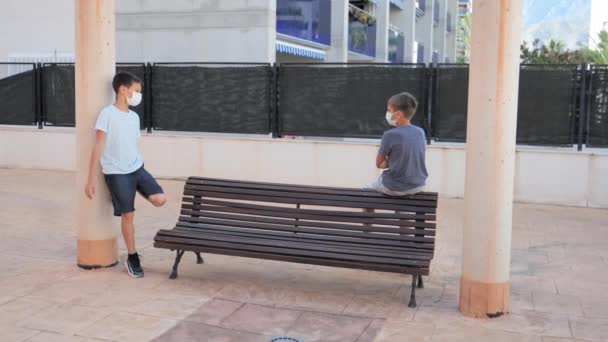 Children with medical protective masks talking outdoors. Boys keep the social distancing to prevent virus spread — Stock Video