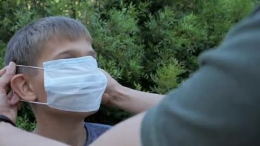 Annesi oğlunun yüzüne koruyucu maske takıyor. Tıbbi koruyucu maskeli çocuk. Sağlık ve güvenlik kavramı, enfeksiyon, virüs koruması