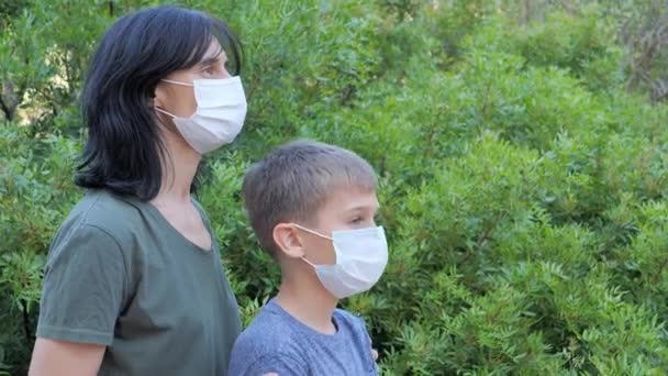 Matka a dítě s lékařskými ochrannými maskami stojící v parku nebo lese za slunečného dne — Stock video