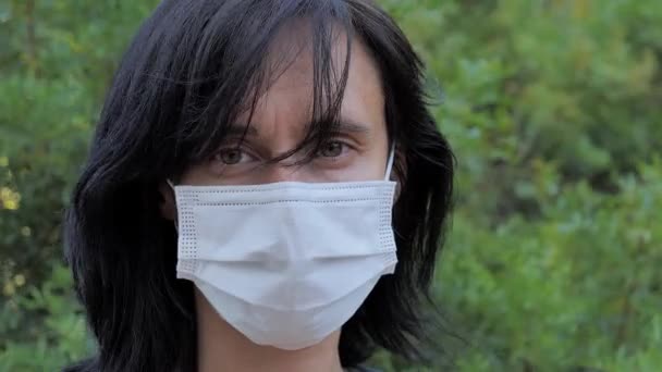Portrét bělošky v lékařské masce, dívající se do kamery a obracející se obličejem ke straně. Žena stojící venku v městském parku — Stock video
