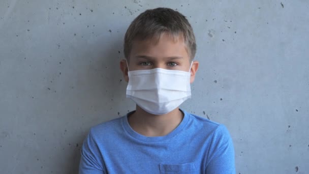 Chlapec s lékařskou ochrannou maskou se dívá do kamery a otočí hlavu na stranu. Dítě stojící u šedé zdi Grunge — Stock video