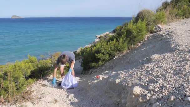 Pulizia della natura, stop plastica, concetto ambientale. Bambino volontario solleva e getta spazzatura di plastica nel sacchetto per riciclare vicino al mare nella giornata di sole — Video Stock