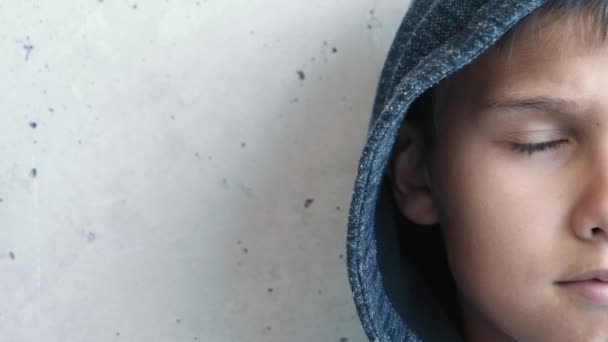 Junge mit Kapuze blickt direkt in die Kamera. Halb Gesicht. Kind nahe grunzgrauer Wand — Stockvideo