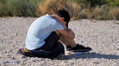 Üzgün, yalnız, mutsuz, hayal kırıklığına uğramış çocuk yerde tek başına oturuyor. Açık havada.