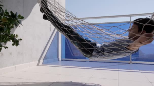 Kind leggen en ontspannen in hangmat opknoping op balkon van appartement. Achteraanzicht. Kind swingend en dromend, denkend — Stockvideo