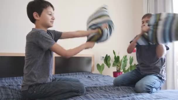 Bambini felici che giocano a lotta cuscino sul letto in camera da letto. I bambini si divertono godendo gioco divertente. Soggiorno a casa di intrattenimento — Video Stock