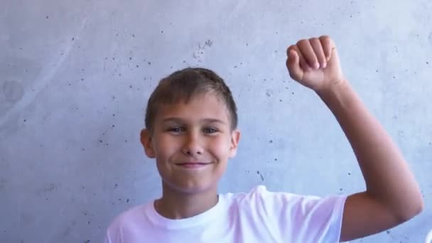 Portrait d'un garçon souriant heureux qui s'amuse à danser avec des mains levantes près d'un mur gris clair — Video