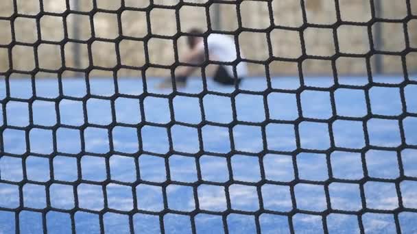 Droevige eenzame jongen bedekte zijn gezicht met handen buiten op de grond. Uitzicht door het tennisnet — Stockvideo