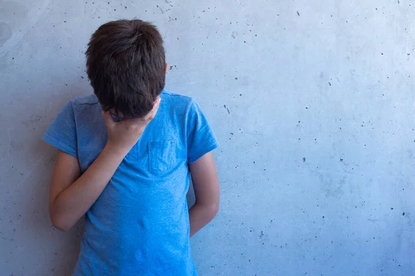 Upprörd ledsen pojke stå ensam och lutar sig mot grå vägg. Inlärningssvårigheter, familjeproblem, mobbning, depression, stress eller frustration — Stockfoto