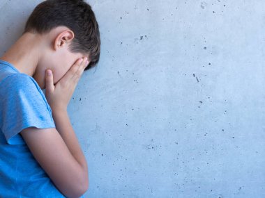 Üzgün çocuk tek başına duruyor ve gri duvara yaslanıyor. Öğrenme güçlüğü, aile sorunları, zorbalık, depresyon, stres veya hüsran kavramı