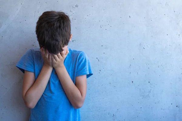 Muchacho triste molesto de pie solo y apoyado en la pared gris. Dificultades de aprendizaje, problemas familiares, bullying, depresión, estrés o concepto de frustración — Foto de Stock