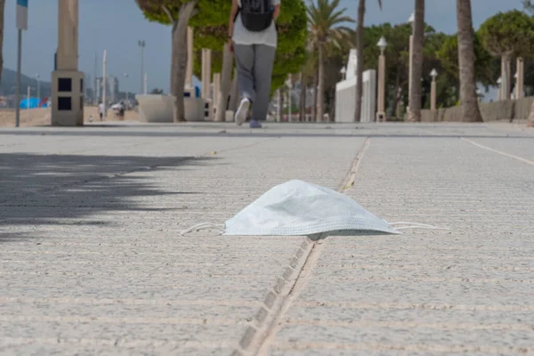 Used lost protective medical face mask on the ground. Disposable face mask lying on the beach promenade. Improperly discarding used face mask