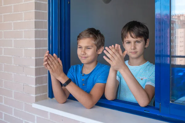 Felices niños sonrientes aplaudiendo desde la ventana para apoyar a doctores, enfermeras, trabajadores hospitalarios durante la cuarentena pandémica del Coronavirus Covid-19 —  Fotos de Stock