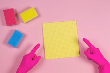 Lastik eldivenli kadın elleri pembe arka plandaki süngerleri işaret ediyor.