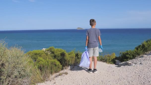 Natuurreiniging, stop plastic, milieuconcept. Vrijwilliger kind verhoogt en gooit plastic afval in de zak voor recycling in de buurt van de zee op zonnige dag — Stockvideo