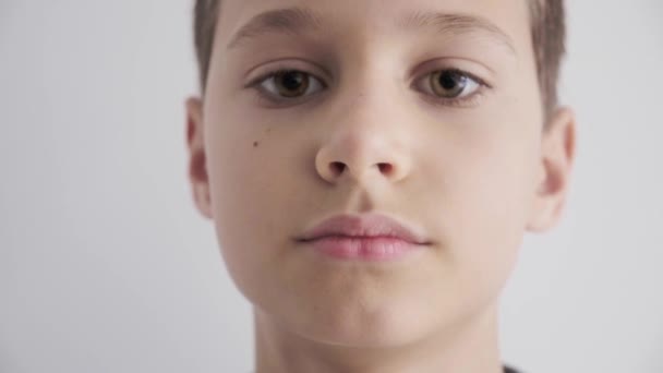 Egy tinédzser fiú portréja, ahogy a kamerába néz. Fiatal, komoly gyerek a kamerába néz. Közelről. Napfény otthon, házon belül. — Stock videók