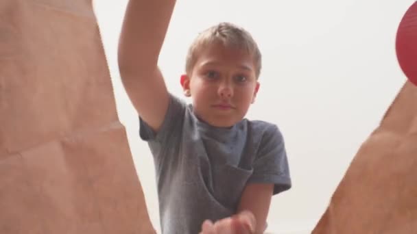 Niño abre bolsa de compras de papel con comestibles comprados para la familia, mira a los alimentos y bienes y saca naranjas frutas — Vídeos de Stock