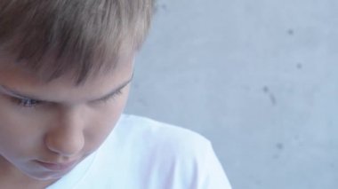 Üzgün, hayal kırıklığına uğramış genç çocuk gri duvarın yanında tek başına dikilip yan tarafa bakıyordu. 4k video